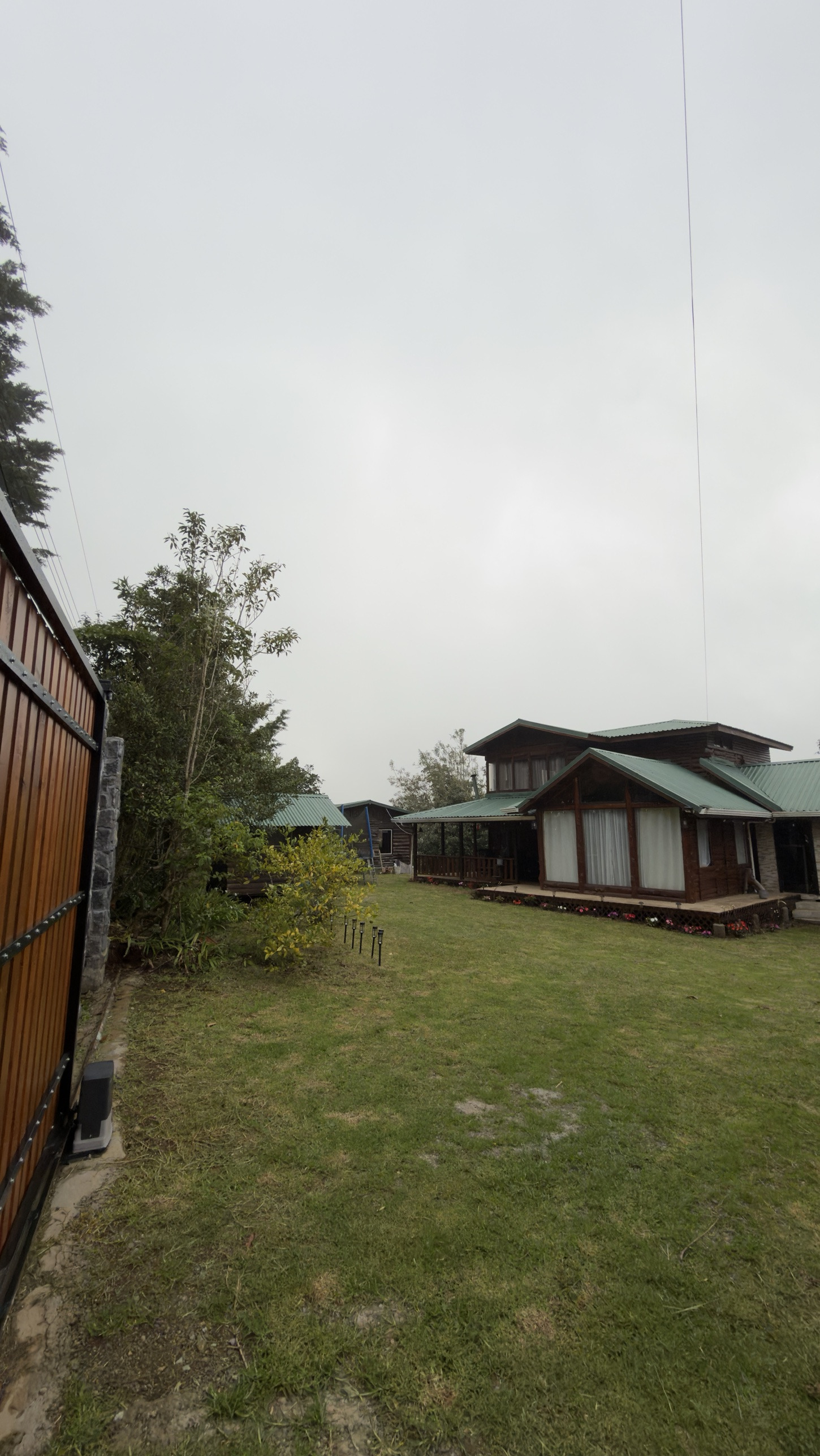 Vista de la finca desde el portón: zacate, la casa principal de madera a la derecha y una casita al fondo