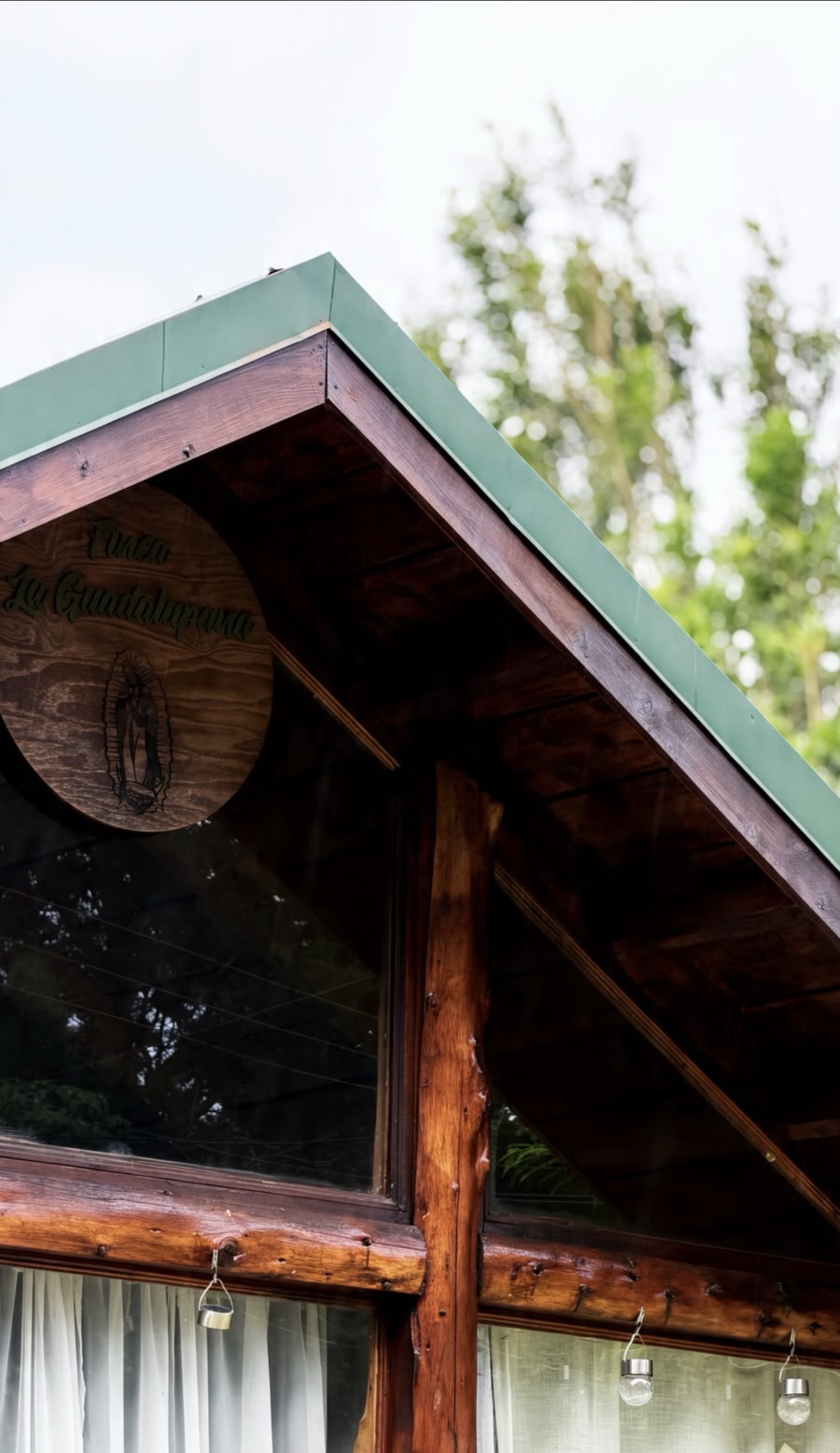 Letrero de madera con la Virgen de Guadalupe y el nombre Finca La Guadalupana, bajo el techo verde de la cabaña