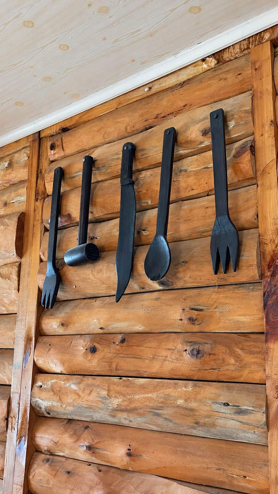 Cubiertos grandes de madera negra colgados en una pared de troncos